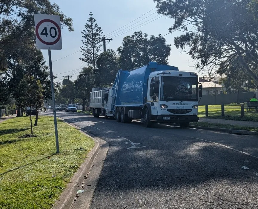 Waste collection vehicle on the residential street beside the reserve